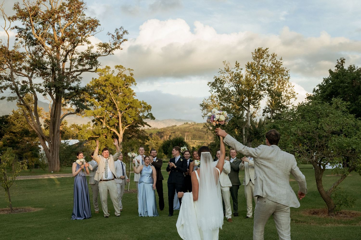 Black and white photo of bride and groom walking hand in hand through lush garden on their wedding day.