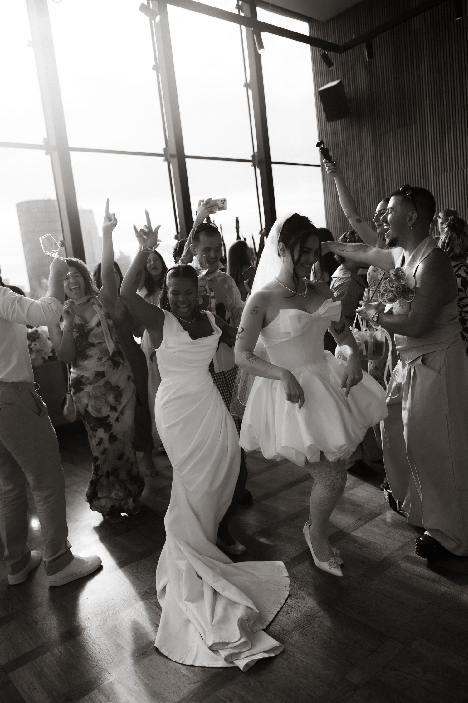 People dancing in a circle at what appears to be a rustic indoor venue with warm lighting and casual atmosphere.