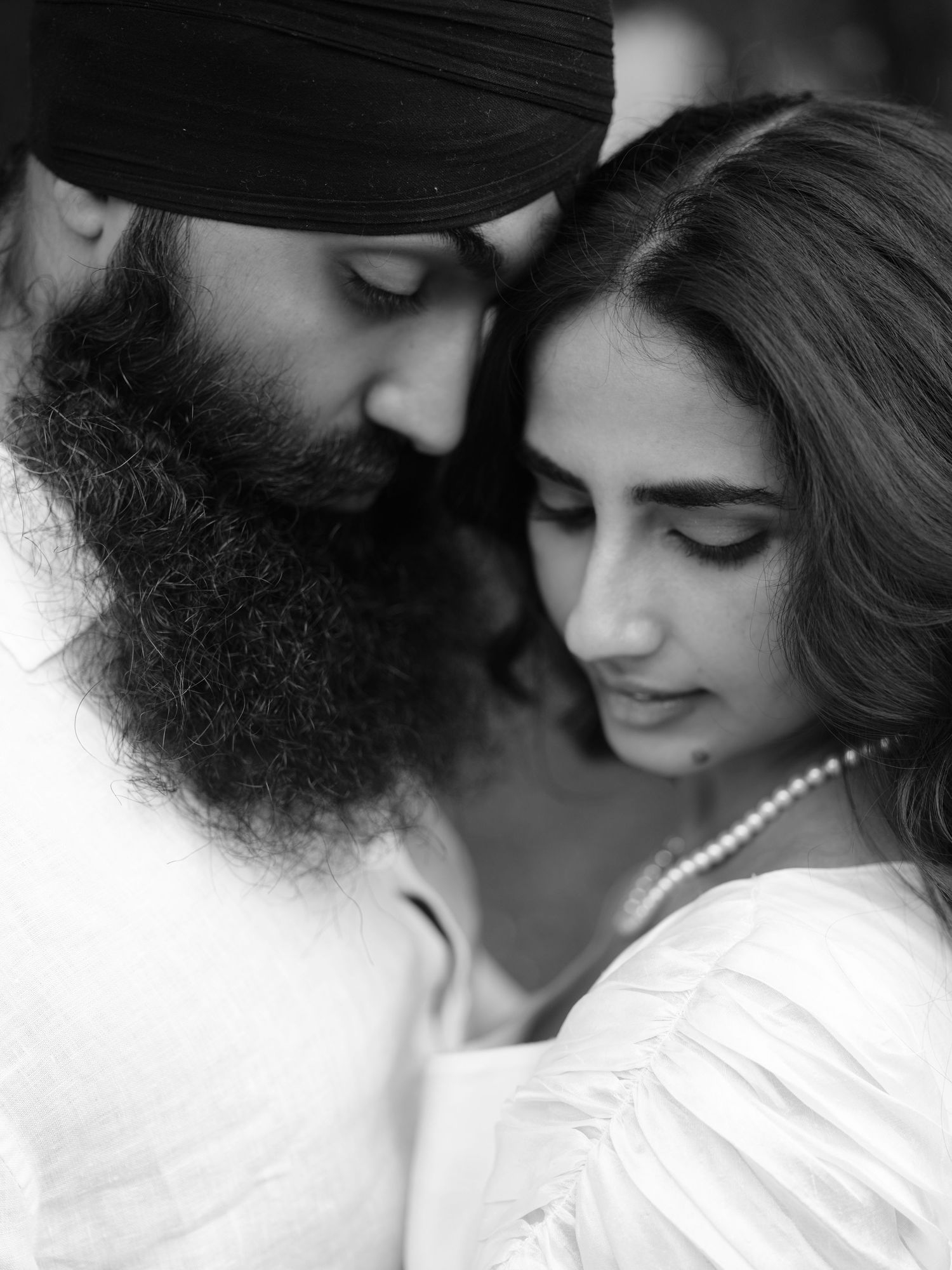 Black and white portrait of a Sikh couple in an intimate, tender moment, man wearing turban with beard, woman in white dress.