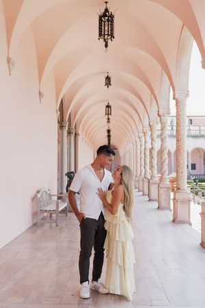Couple sharing a tender moment under pink arched colonnade with ornate columns.