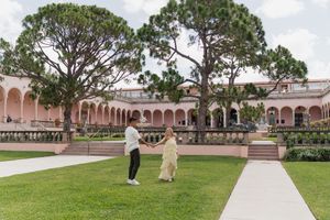 Newly engaged couple dancing on lawn of pink Mediterranean Revival museum courtyard.