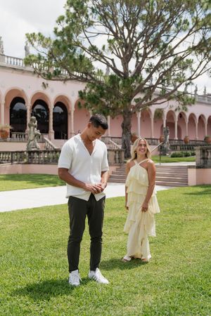 Couple standing on grass lawn in front of elegant pink arched building on sunny day.
