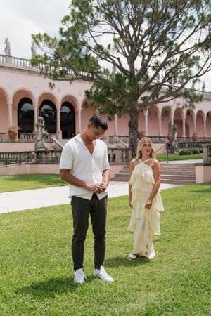 Man nervously preparing to propose while woman approaches in elegant garden courtyard.