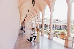 Man proposing to woman in elegant arched colonnade of historic building with marble columns and courtyard.