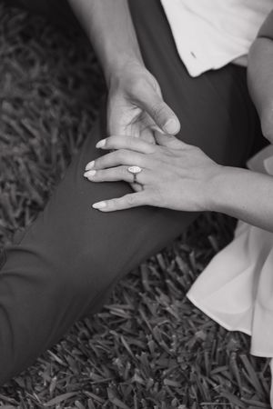 Close-up black and white photo of an engaged couple holding hands, showcasing a beautiful oval engagement ring.