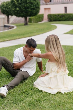 Man kissing womans hand while sitting together on green lawn at elegant estate.