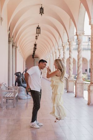 Newly engaged couple celebrating under elegant pink arched colonnade with sculptures.