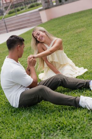 Happy couple sitting on green lawn holding hands and laughing together outdoors.