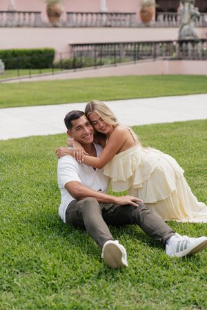 Happy couple embracing on lawn, woman in yellow ruffled dress hugging smiling man in white shirt.