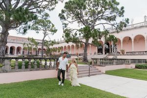 Happy newly engaged couple walking through lush garden of pink Mediterranean estate.