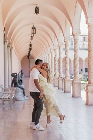 Romantic couple embracing and dancing in stunning pink arched corridor with classical columns.