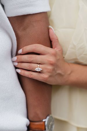 Close-up of a woman's hand with a marquise diamond engagement ring, resting on a man's arm.