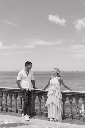 Black and white photo of a couple on a balcony overlooking the ocean.