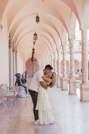 Couple sharing first kiss as newly engaged pair in beautiful pink arched colonnade.