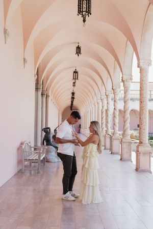 Couple holding hands in an elegant arched pink corridor with marble columns.