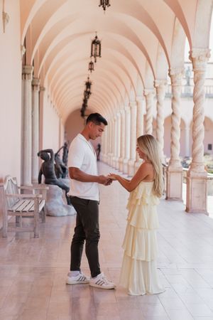 Couple holding hands and sharing an intimate moment in a beautiful pink arched hallway with marble columns.