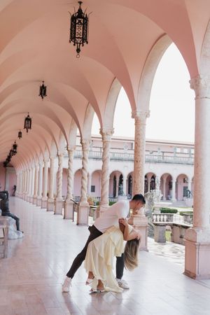 Couple sharing a romantic dip kiss under elegant pink arched colonnade.