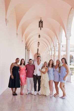 Group of eight friends posing and smiling together in a stunning pink arched colonnade with ornate columns.