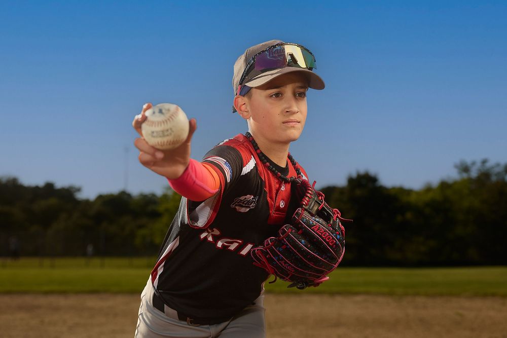 Young baseball pitcher in red uniform poses with ball ready to throw on outdoor field.
