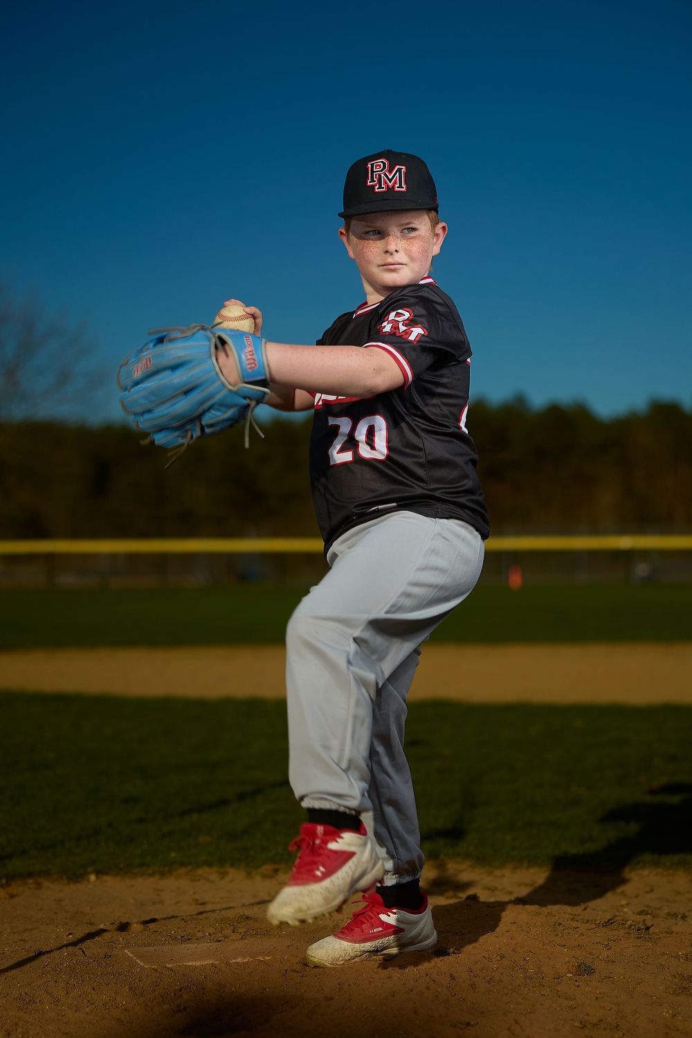 Young baseball pitcher in number 20 jersey winds up on the mound during a youth league game on a sunny day.