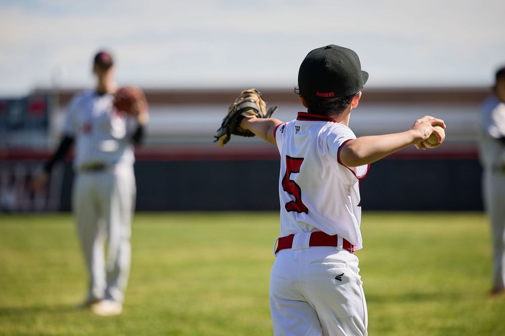 Young baseball player in white uniform winding up to throw a ball during a youth league game on a sunny day.