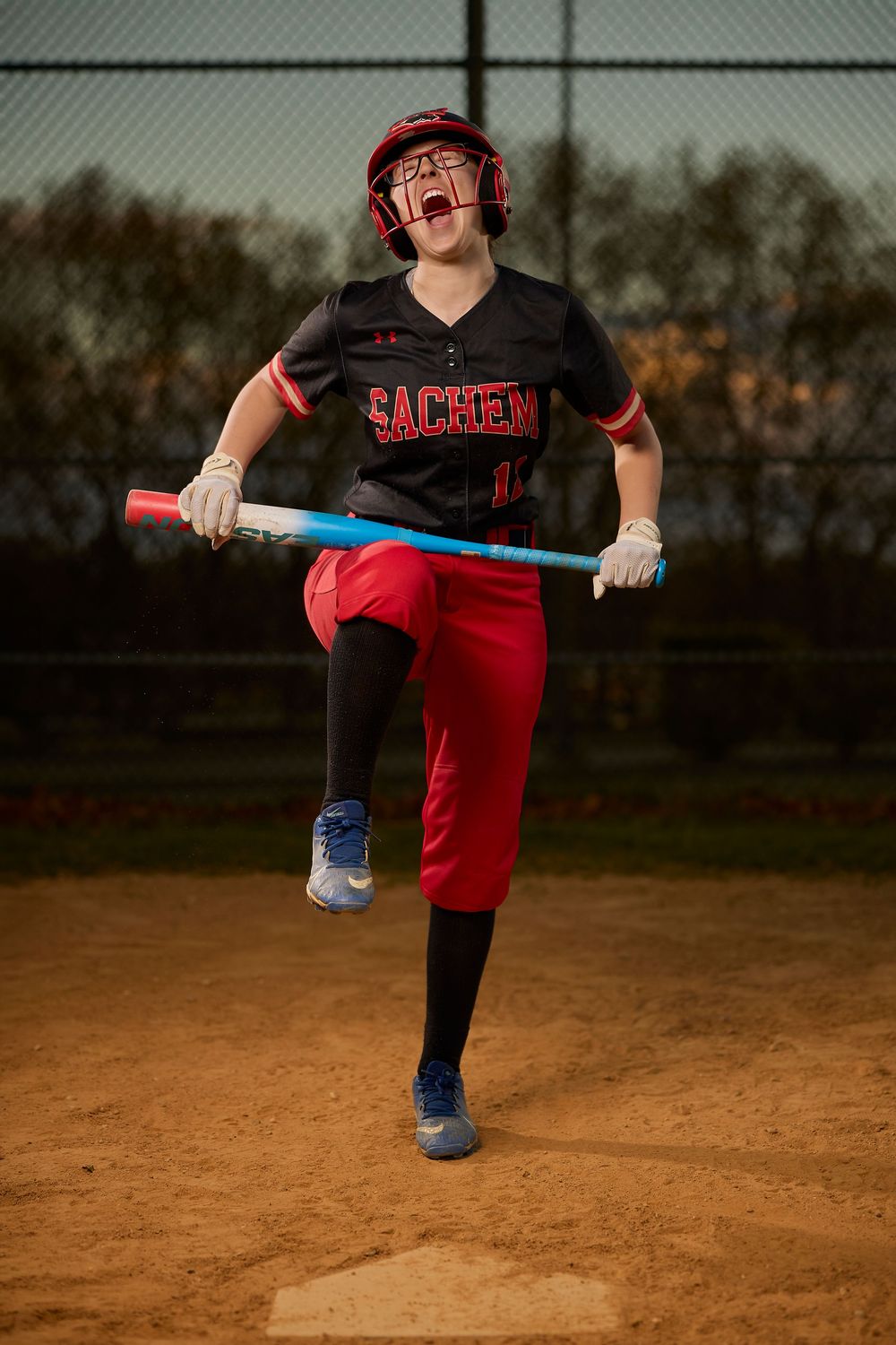 Excited Sachem softball player in red helmet celebrates while holding a colorful bat on the field.