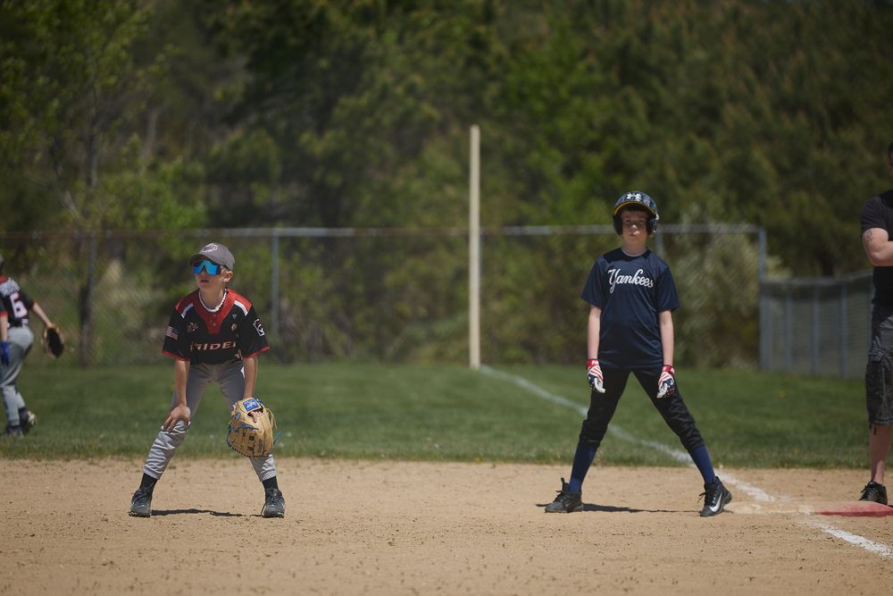 Youth baseball players in action on a dirt field, with a batter and fielder ready during a little league game.