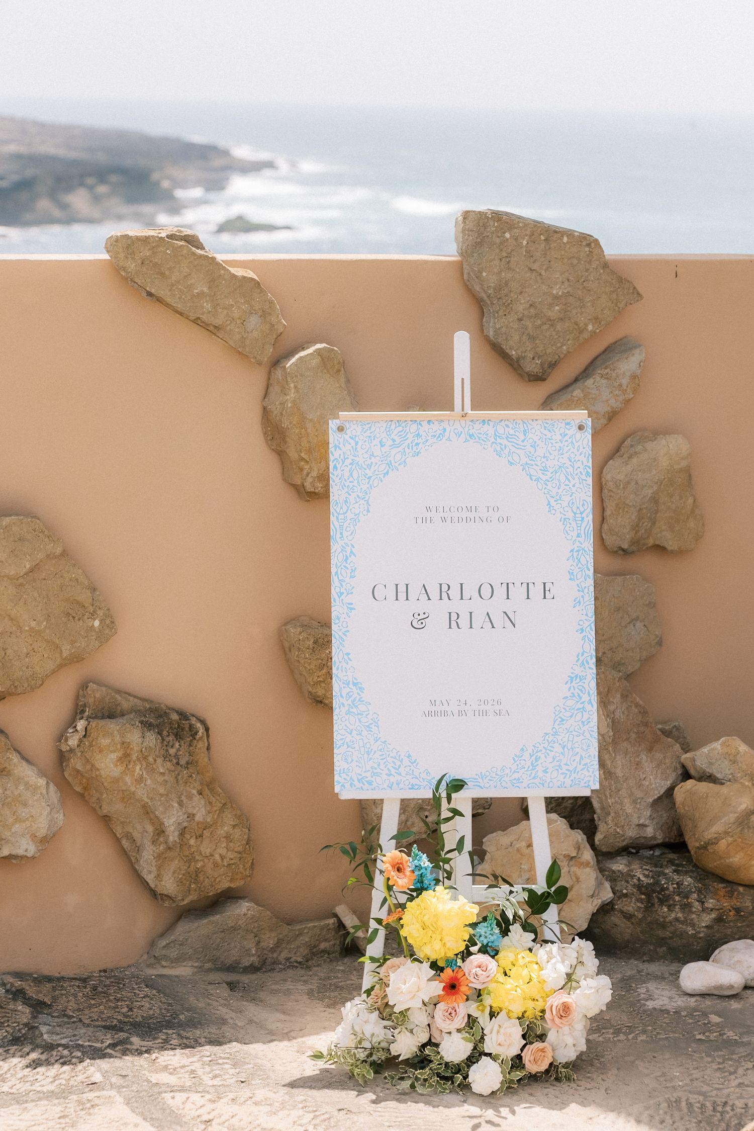 Coastal wedding welcome sign decorated with fresh flowers for an oceanfront wedding at Arriba by the Sea in Portugal.