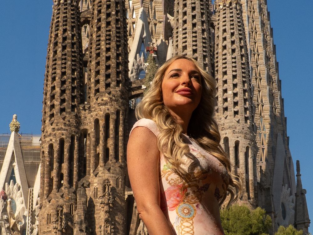 Blonde woman posing in front of Sagrada Familia basilica in Barcelona on a sunny day.
