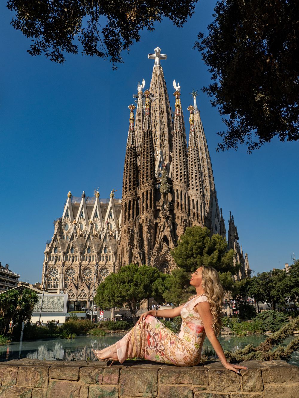 Woman in floral dress posing by Sagrada Familia basilica in Barcelona, Spain on a sunny day.