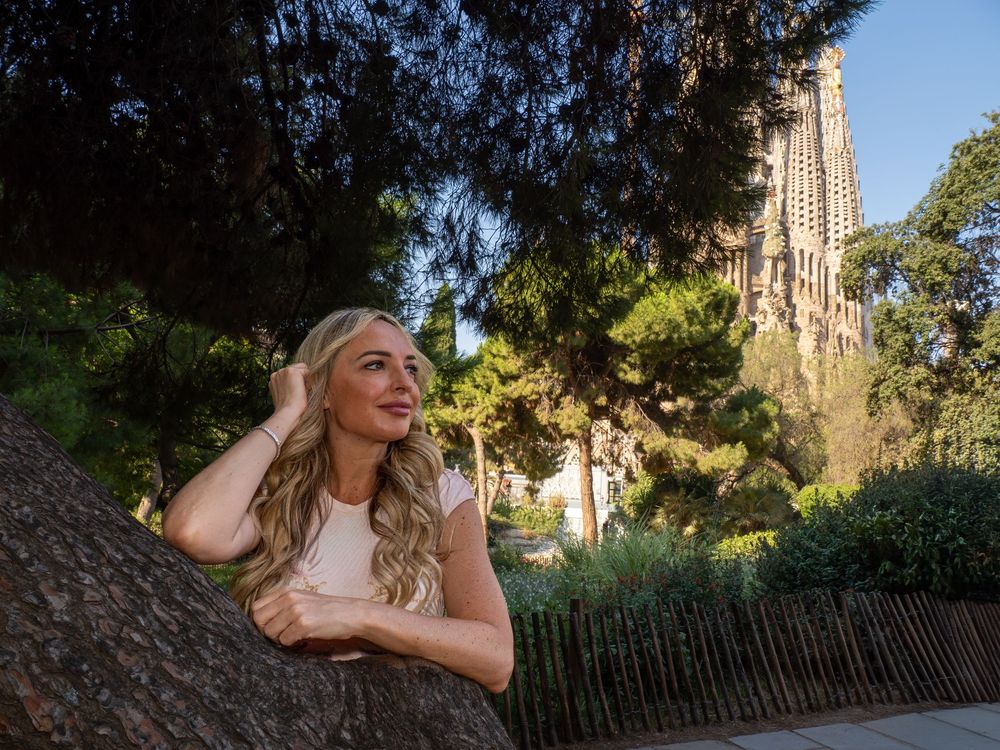 Blonde woman posing by a tree with Sagrada Familia basilica in background, Barcelona, Spain.