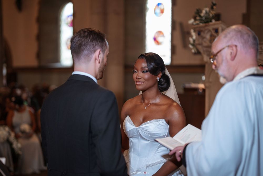 Bride and groom exchange vows at church altar during wedding ceremony with officiant holding book.