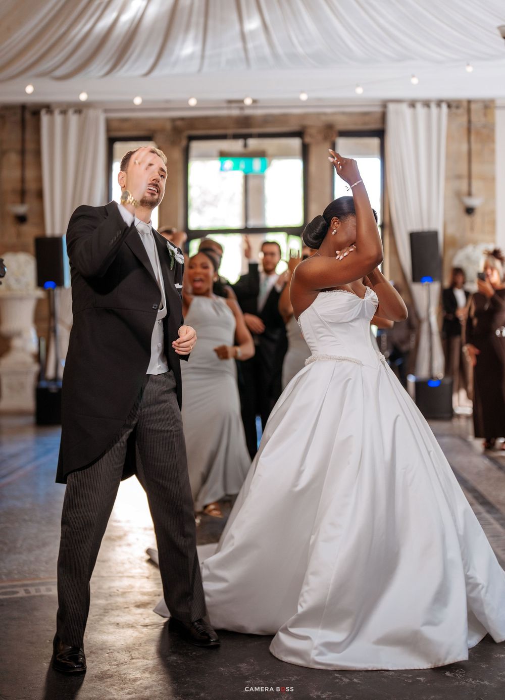 Bride in white gown and groom in black suit share joyful first dance at elegant wedding reception.