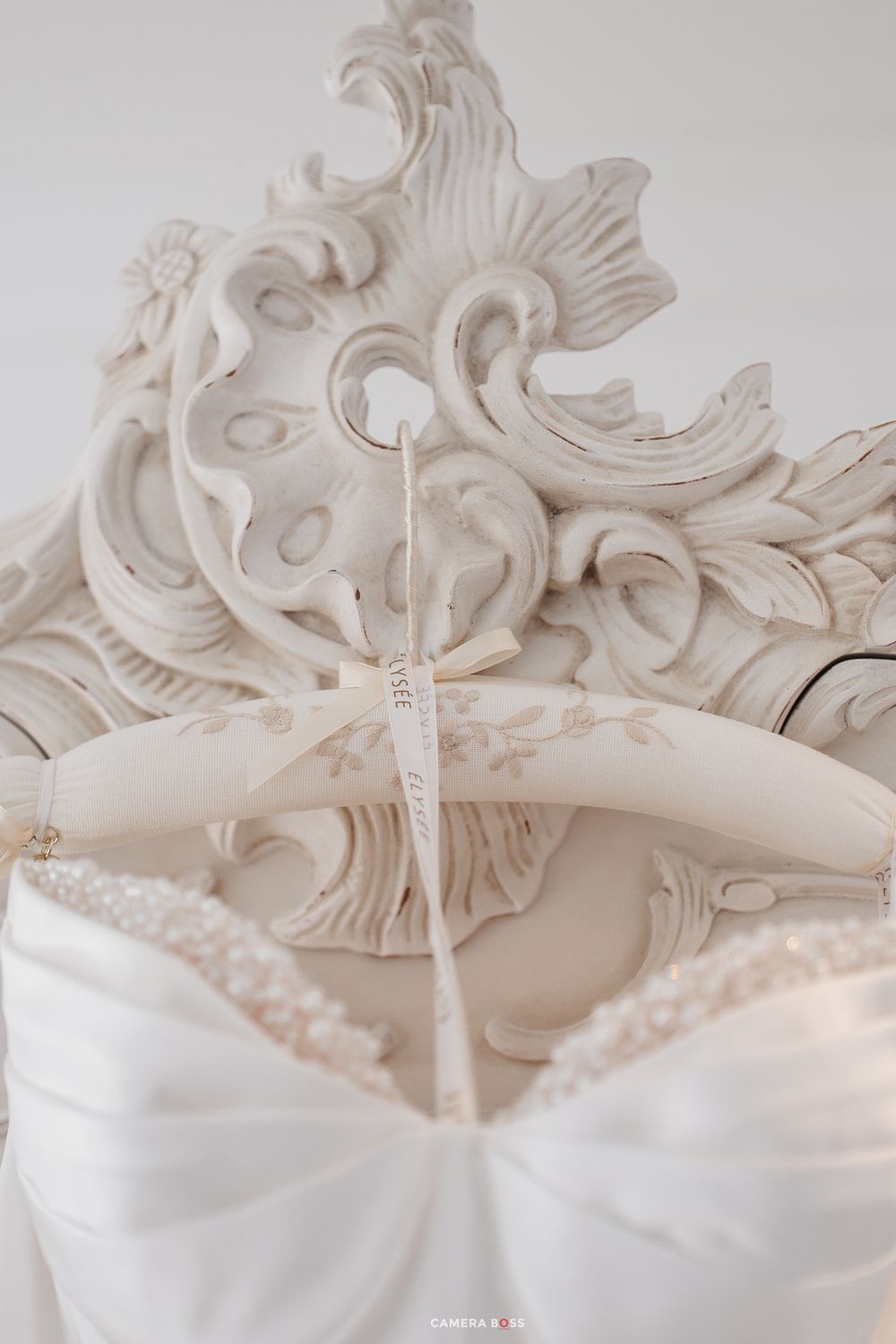 Ornate white baroque mirror with decorative wedding dress hanger and beaded bridal gown detail.