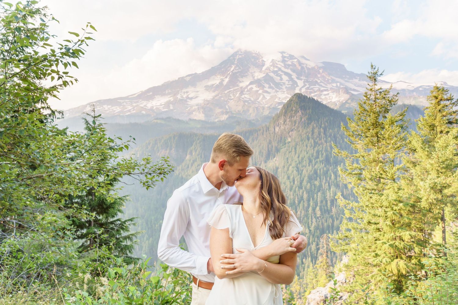 Couple kissing in front of Mount Rainier surrounded by evergreen trees on a beautiful wedding day.