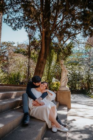 Playful couple sharing an inside joke on a stone bench in the quiet, empty gardens of Jardin Julio Munoz
