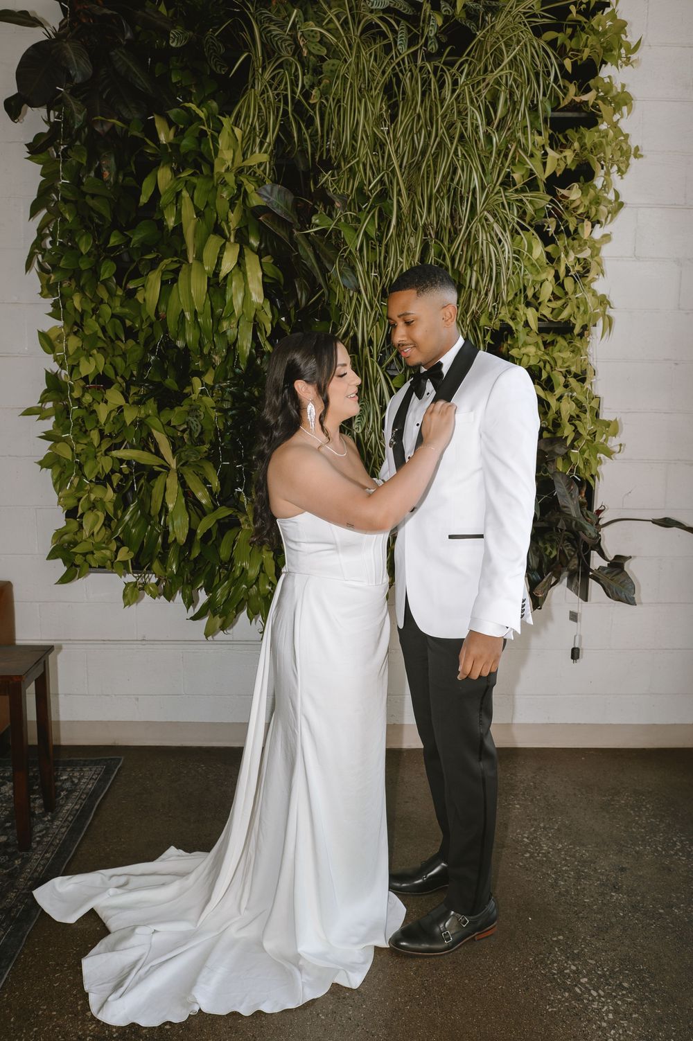 Bride and groom share romantic moment before lush green plant wall at modern wedding ceremony.