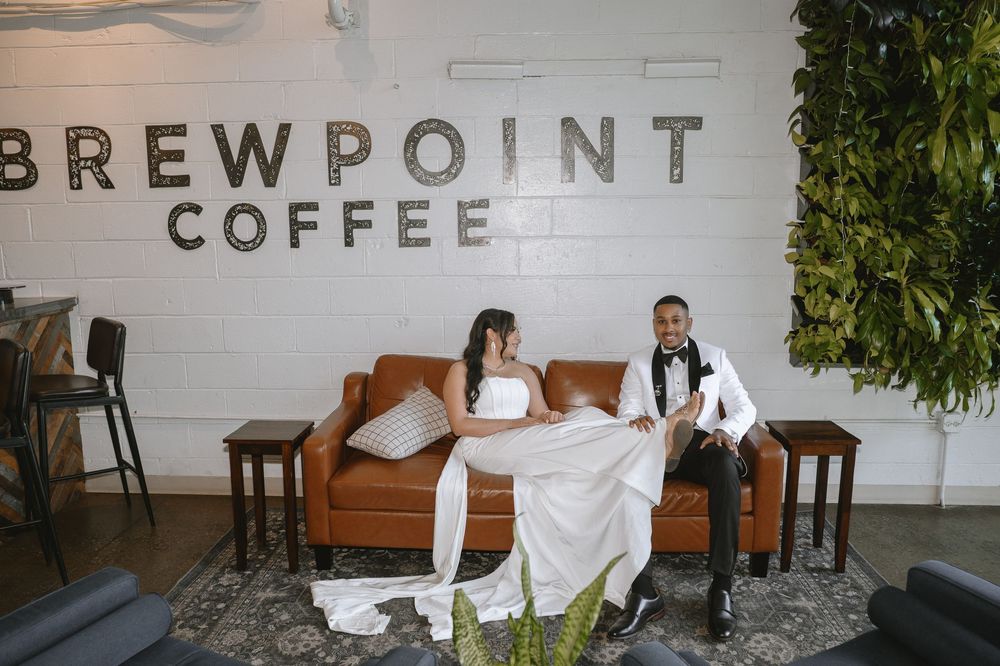Bride and groom sitting on a brown leather couch at Brewpoint Coffee shop on their wedding day.