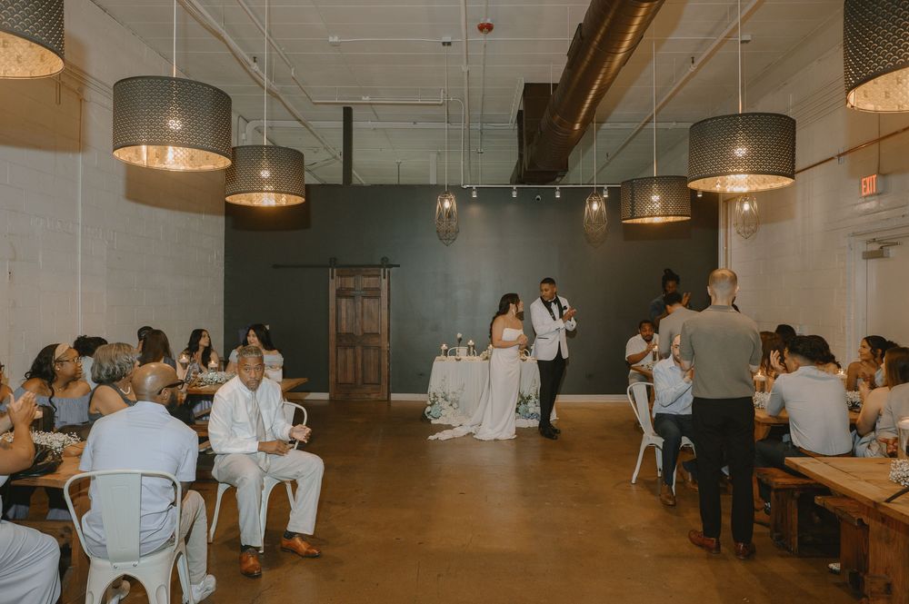 Bride and groom share first dance in elegant industrial wedding venue with pendant lights and seated guests.