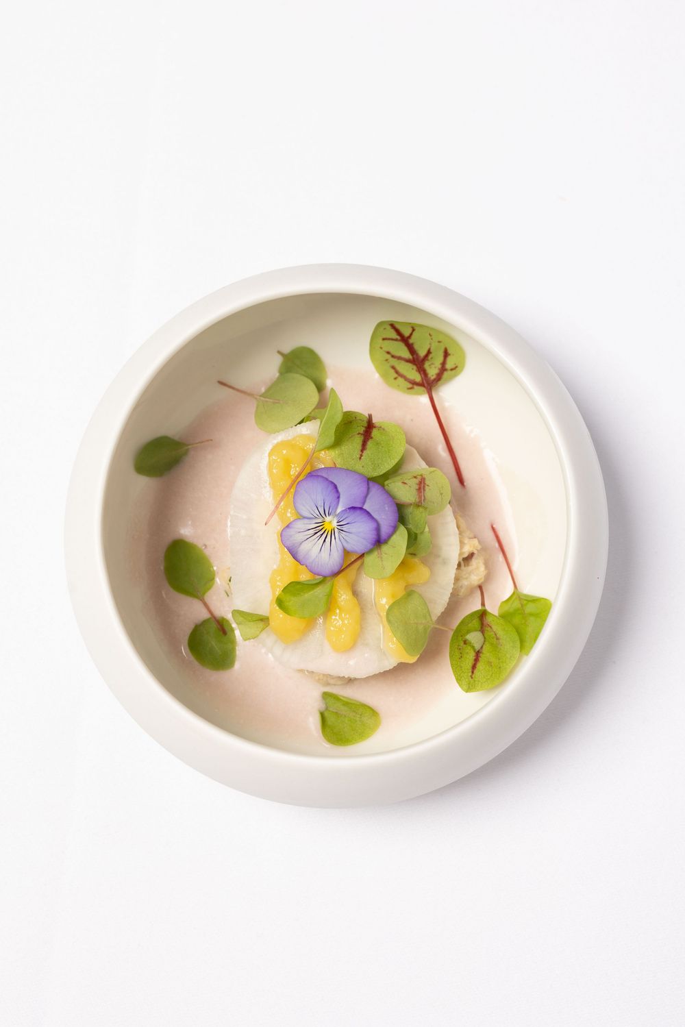 A series of white ceramic bowls containing delicate edible flowers and microgreens arranged in a minimalist style.