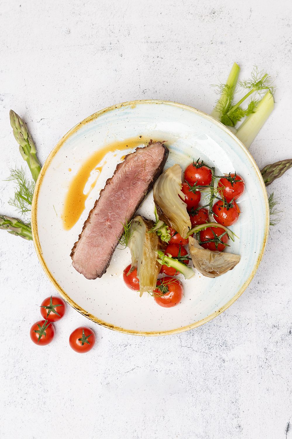 Gourmet plated medium-rare duck breast with roasted cherry tomatoes, fennel and asparagus on a white ceramic plate.