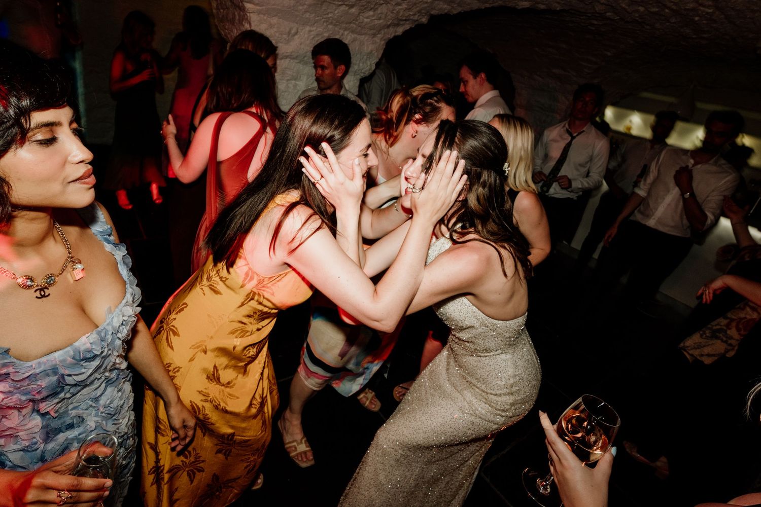 Guests dancing and celebrating at a lively wedding reception party in a dimly lit venue.