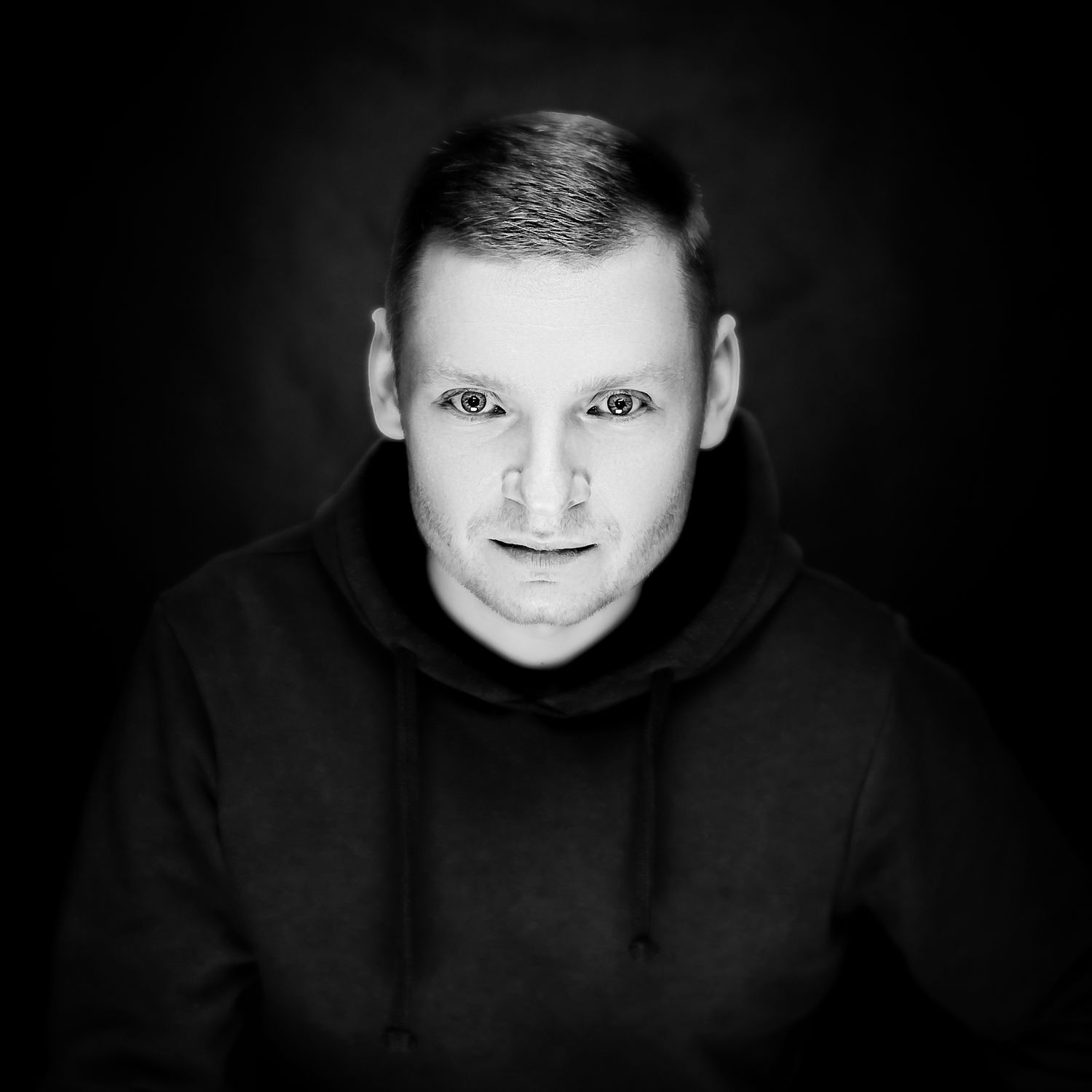 A monochrome self-portrait of Krystian Falkowski, fine art photographer, wearing a minimalist black hoodie and looking focused.
