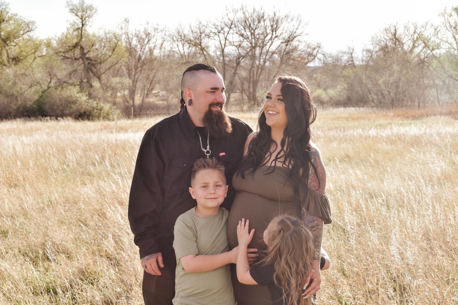 A happy family of six sits together in a grassy outdoor setting with red rocks and trees in the background.