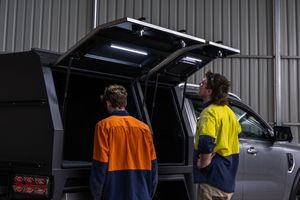 Two workers in hi-vis shirts inspect a custom aluminium ute canopy with LED lighting in a workshop.