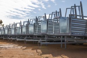 Rows of fabricated steel frames and panels stored outdoors on red dirt under a partly cloudy sky.