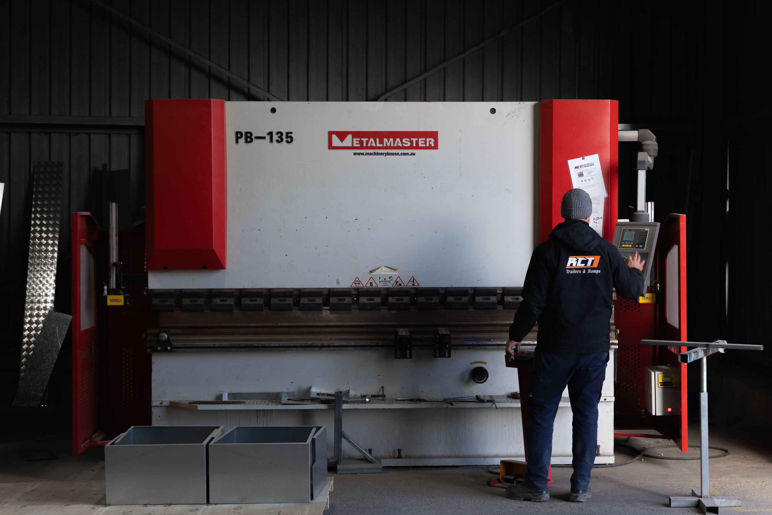 Worker in hi-vis gear operates a Metalmaster PB-135 press brake machine in an industrial workshop.