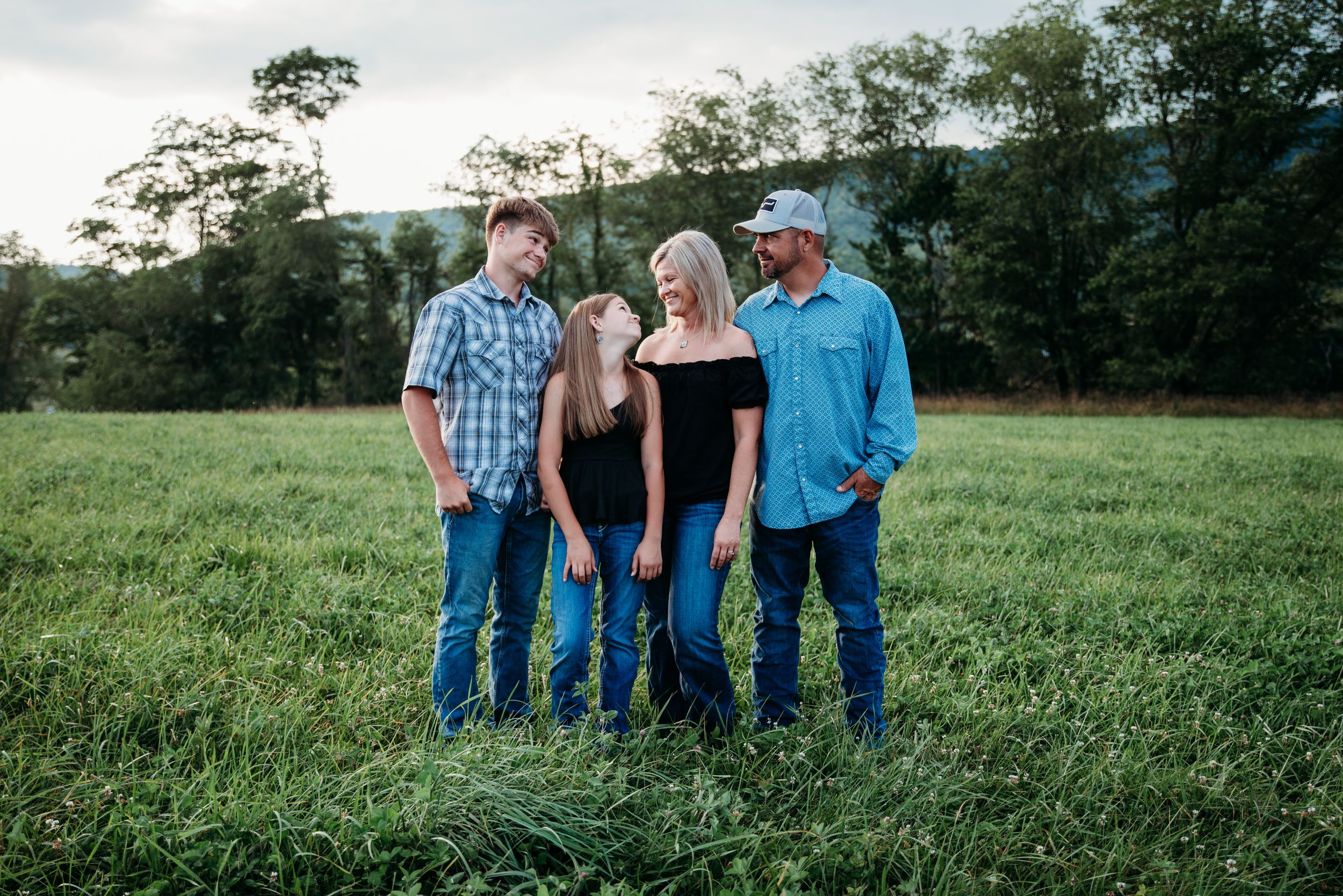 A group stands together in a grassy field at dusk with trees and mountains visible in the background.