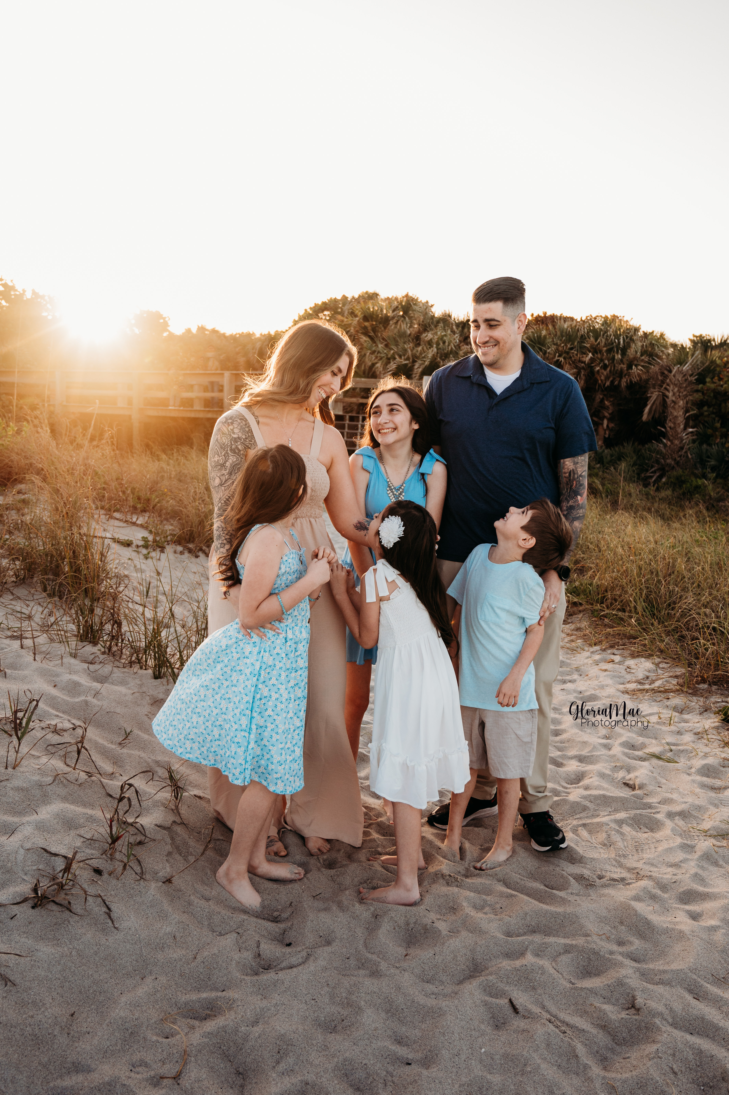 A family shares a joyful moment together on a sandy beach at sunset with golden light filtering through the scene.