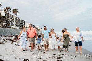 A group walks together along a sandy beach with palm trees and condominiums in the background.